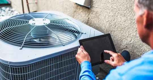 Maintenance technician using digital tablet to inspect air conditioning unit